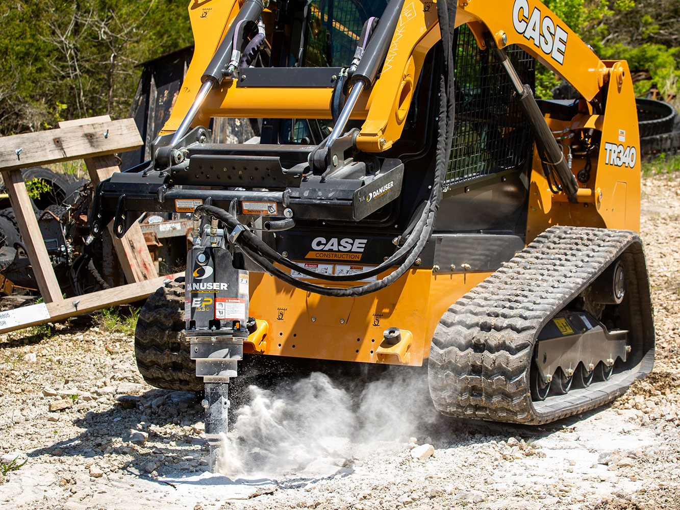 Image showing Danuser EP 1530 Auger Drive on Case TR340 Skid Steer drilling into rocky ground, dust visible during operation