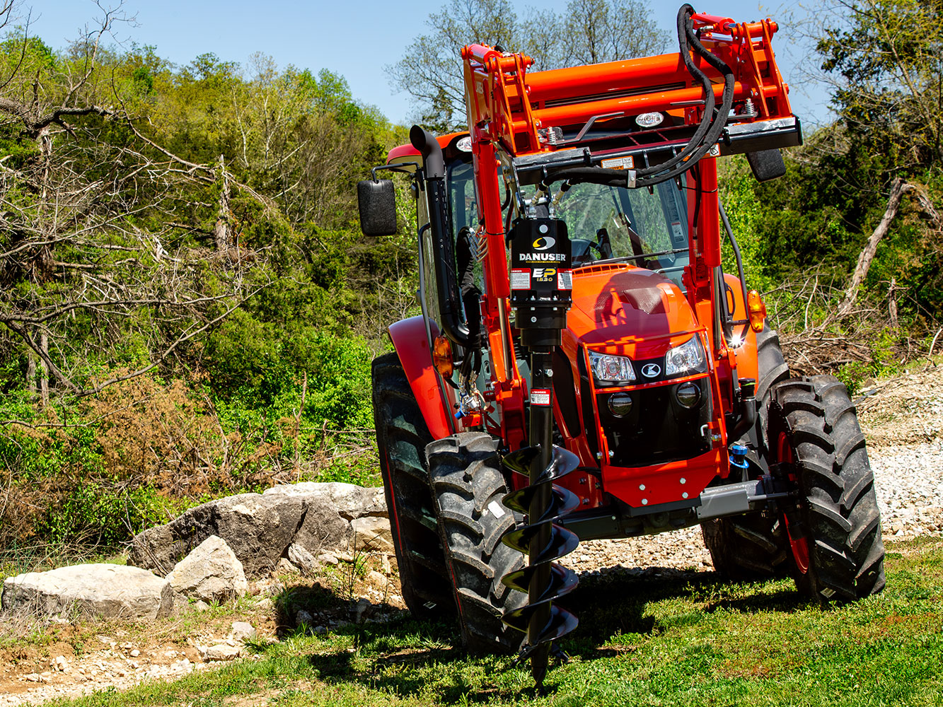 Image showing Danuser EP 1530 Auger Drive on Kubota tractor on grassy and rocky terrain with trees in background
