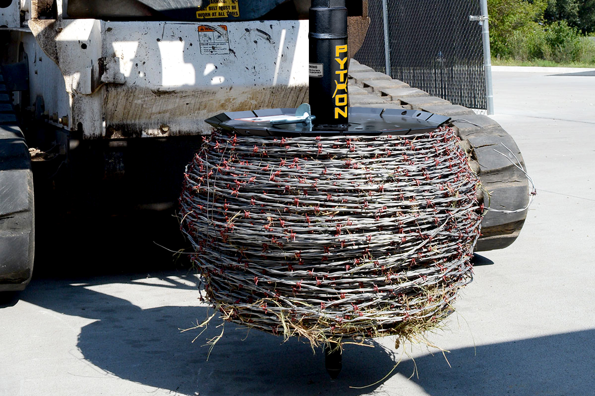 Image showing close-up of Danuser Python Wire Winder on Bobcat T870 with barbed wire and grass entangled on attachment