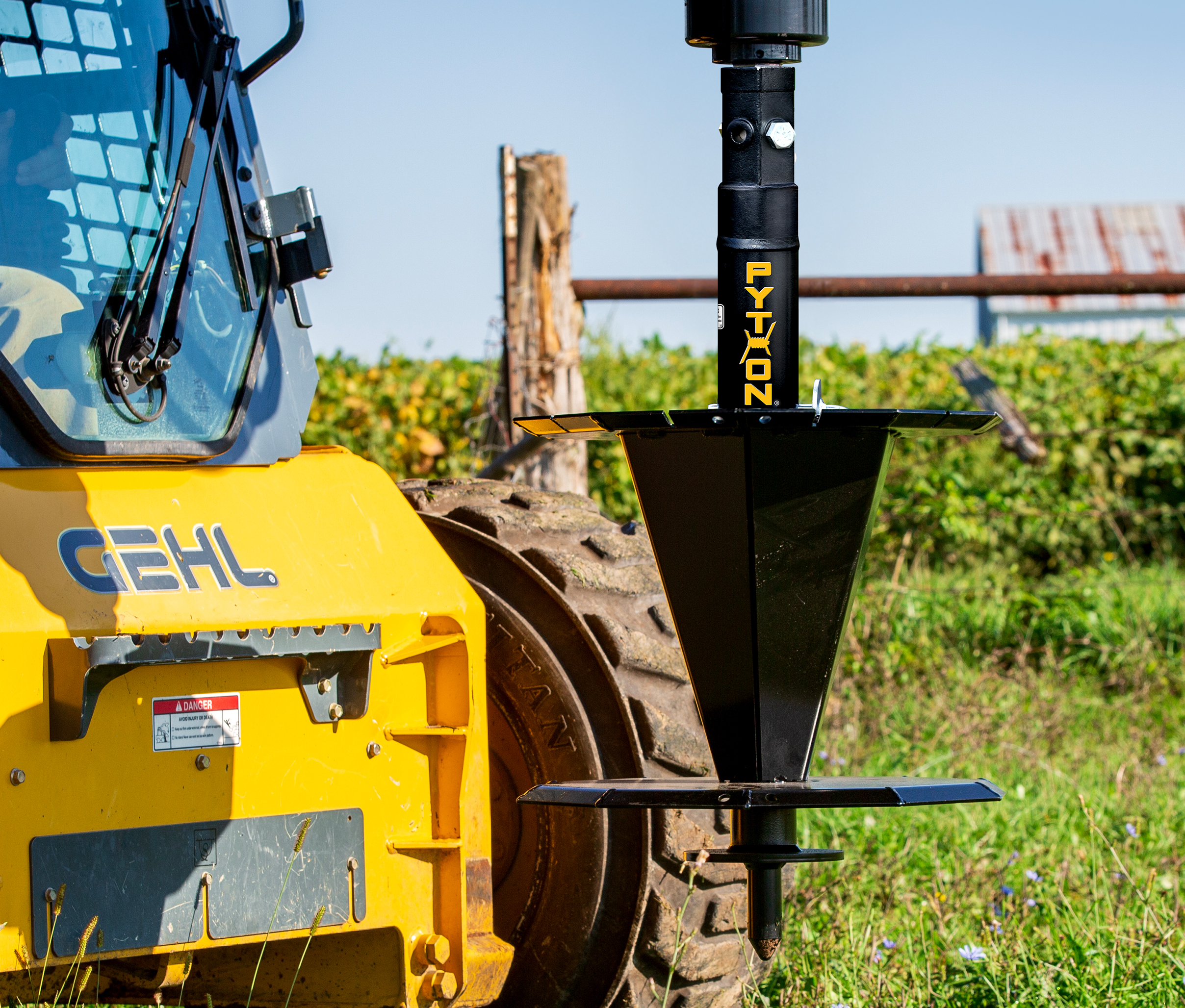 Image showing Close-up of Danuser Python Wire Winder on Gehl skid steer, no wire loaded in green vegetation and rusted-roof structure in background