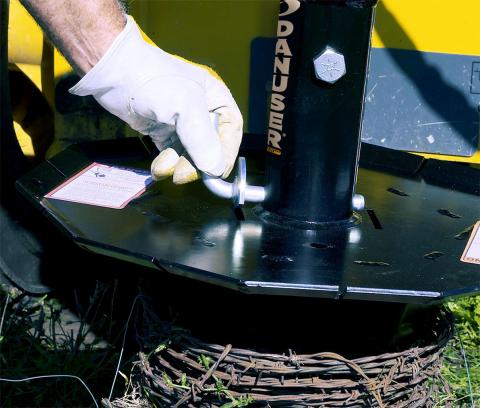 Image showing close-up of Danuser Python Wire Winder with barbed wire and gloved hand adjusting retention pin on black metal part