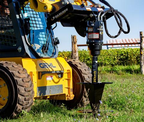 Image showing Danuser Python Wire Winder and EP attachment on Gehl skid steer, no wire, grassy terrain with fence and plants