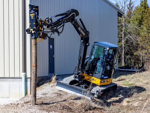 Image showing Danuser Hornet T8-RR post driver using tilt feature on Mini John Deere 50P Excavator holding wood post beside building