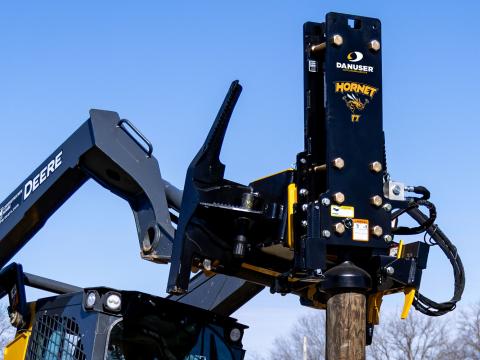 Image showing close-up of Danuser Hornet T7 post driver on John Deere 333G Skid Steer with arm extensions holding wood post in the air