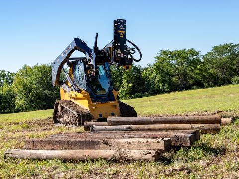 Image shows Danuser Hornet T8-RR post driver on John Deere 333G Skid Steer near wood post pile in open field with trees