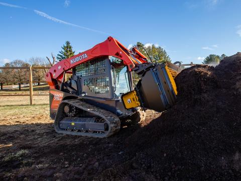 Image showing Danuser Mega Mixer on Kubota SVL 75-2 Skid Steer scooping compost from pile near fence, trees, and blue sky